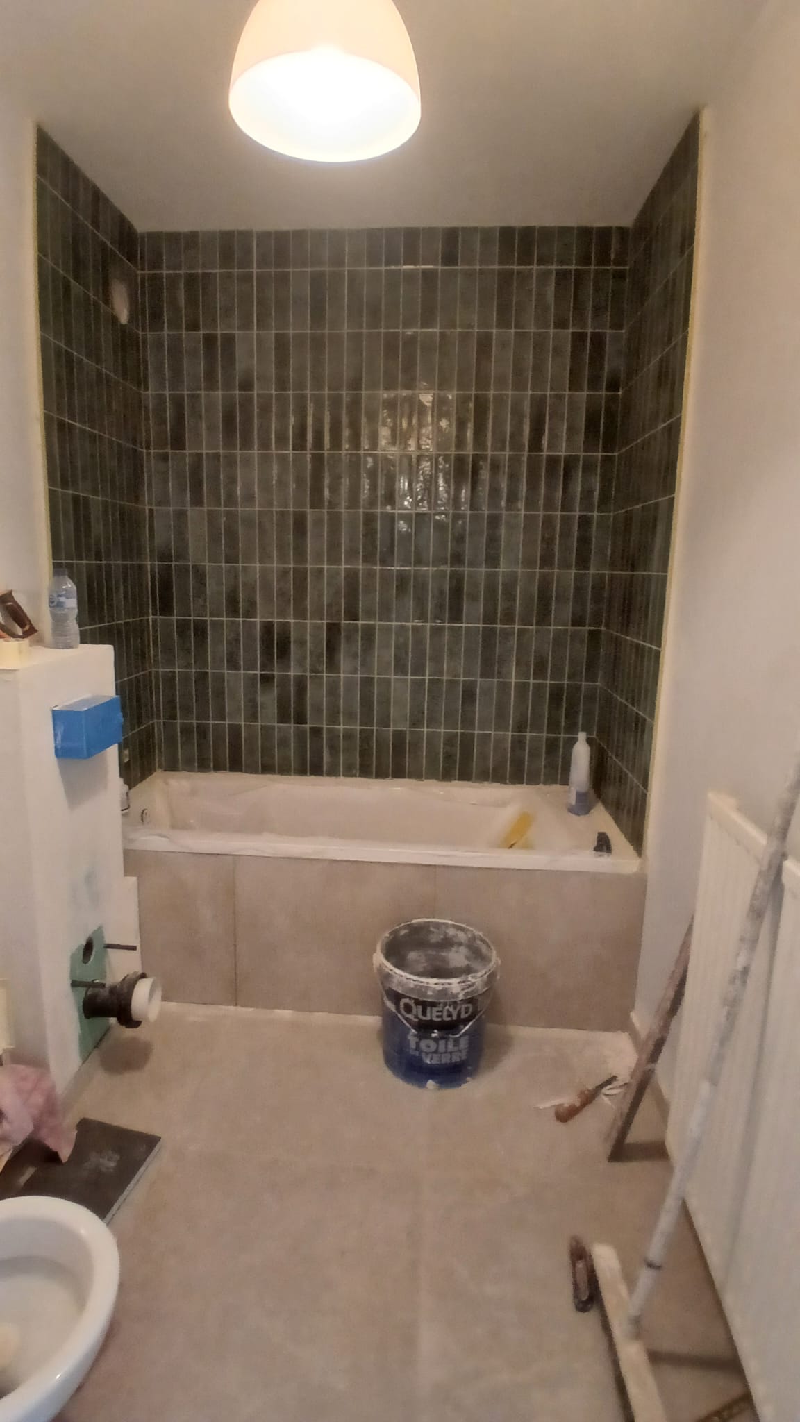 Vue d'ensemble de la salle de bains : baignoire, carrelage vertical et faux-plafond