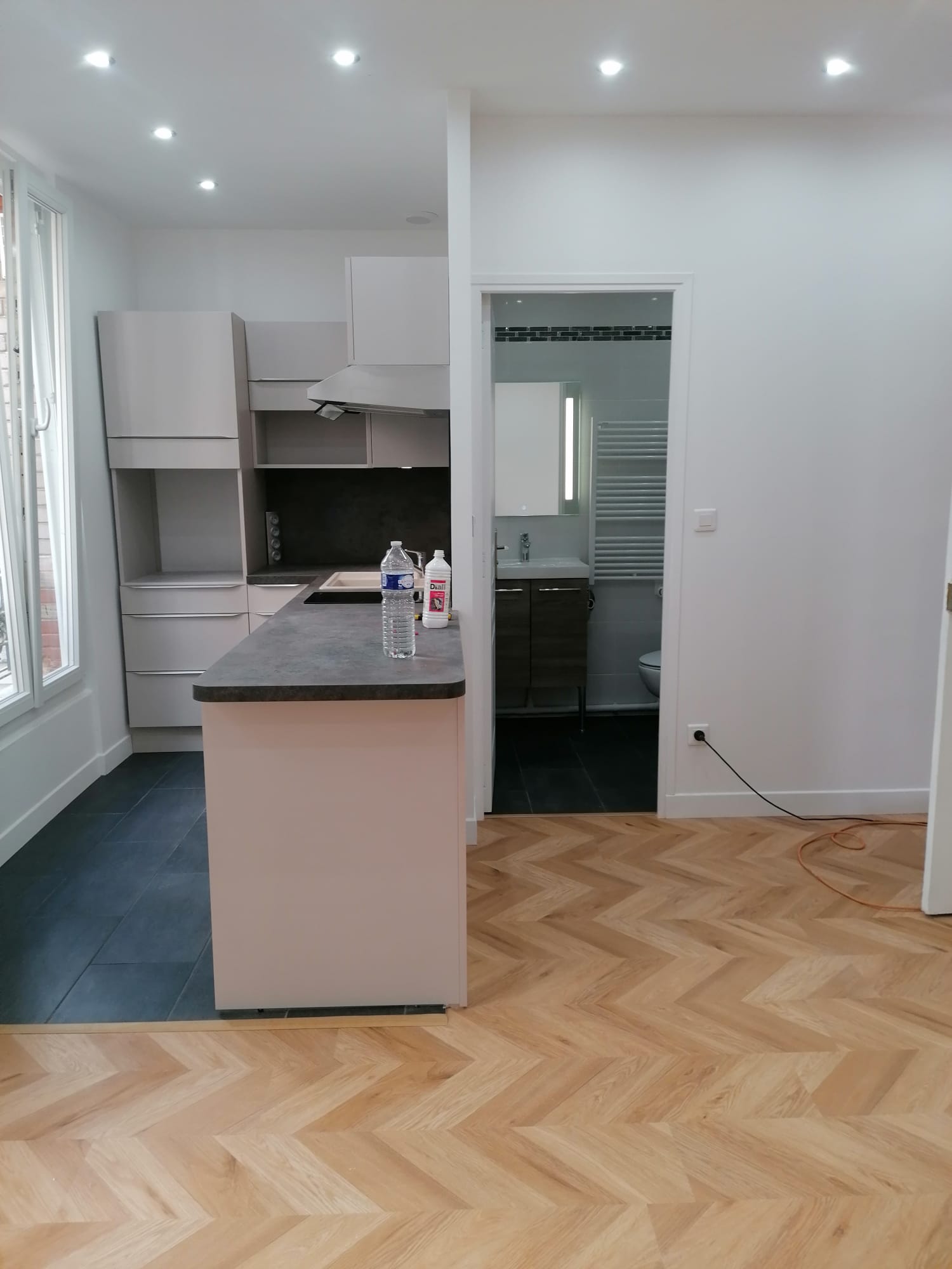 Cuisine ouverte finie à Paris 8e : meubles gris clair, plan effet béton et parquet chevron