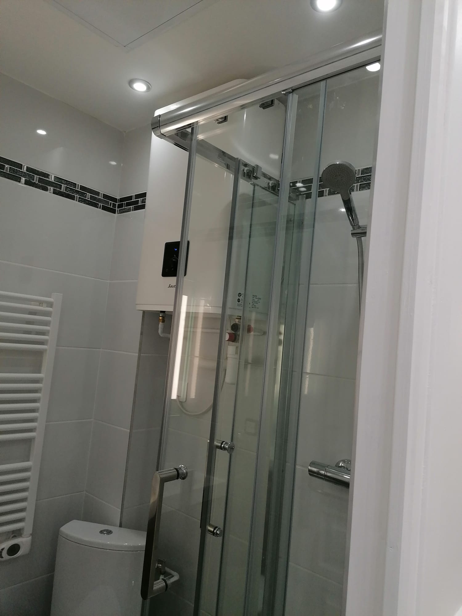 Cabine de douche vitrée, frise mosaïque et chauffe-eau dans la salle d'eau rénovée