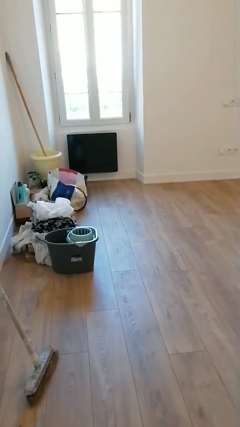 Pièce de vie après travaux : parquet stratifié chêne, murs blancs et radiateur neuf